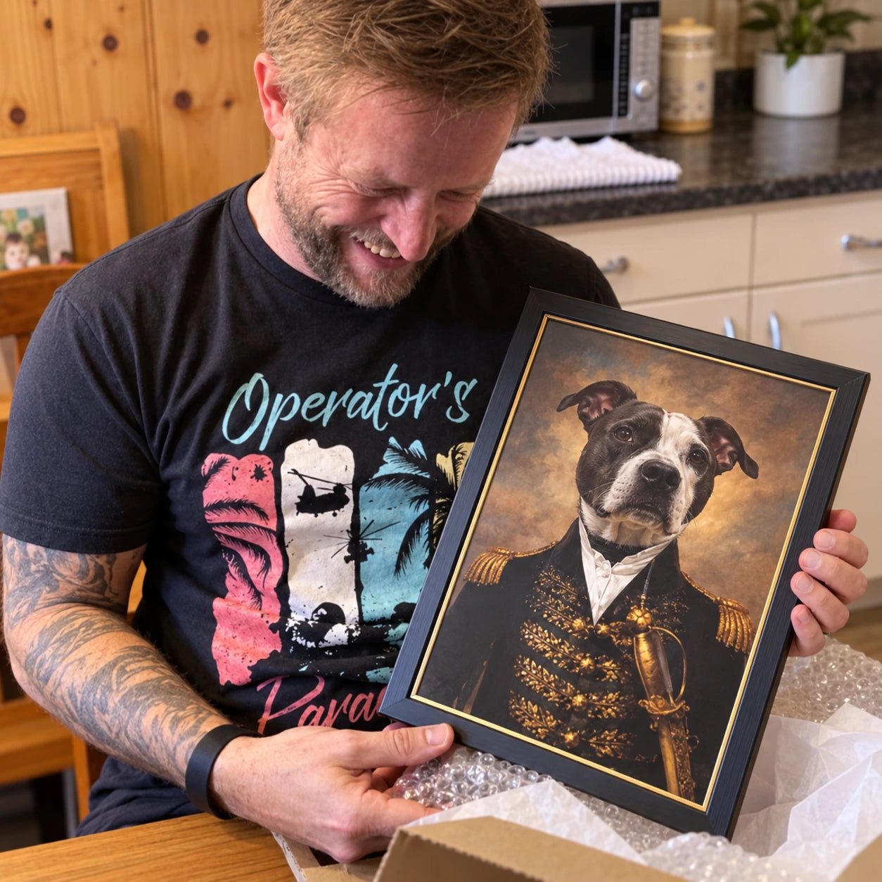A man in a black graphic t-shirt holds up a framed custom pet portrait of a pitbull-type dog dressed as a military general, with a gold-trimmed black frame and a warm sepia background.